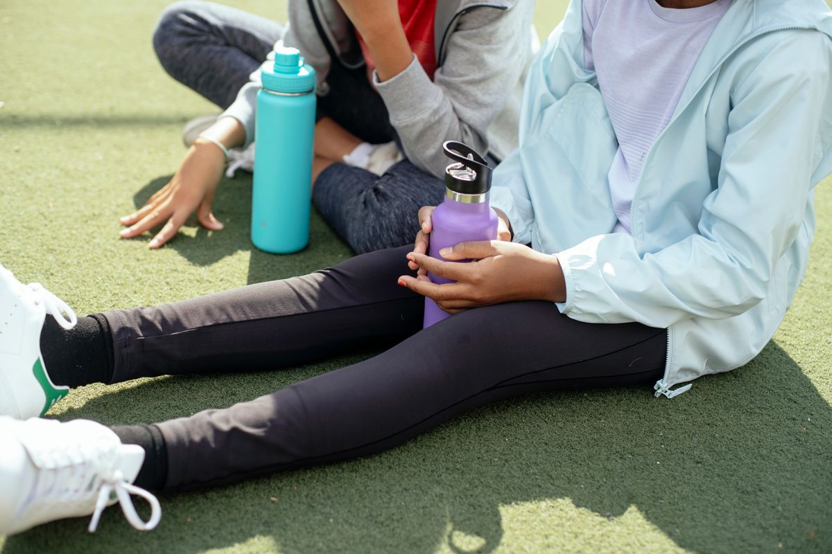 Two insulated kids' water bottles on the grass beside children