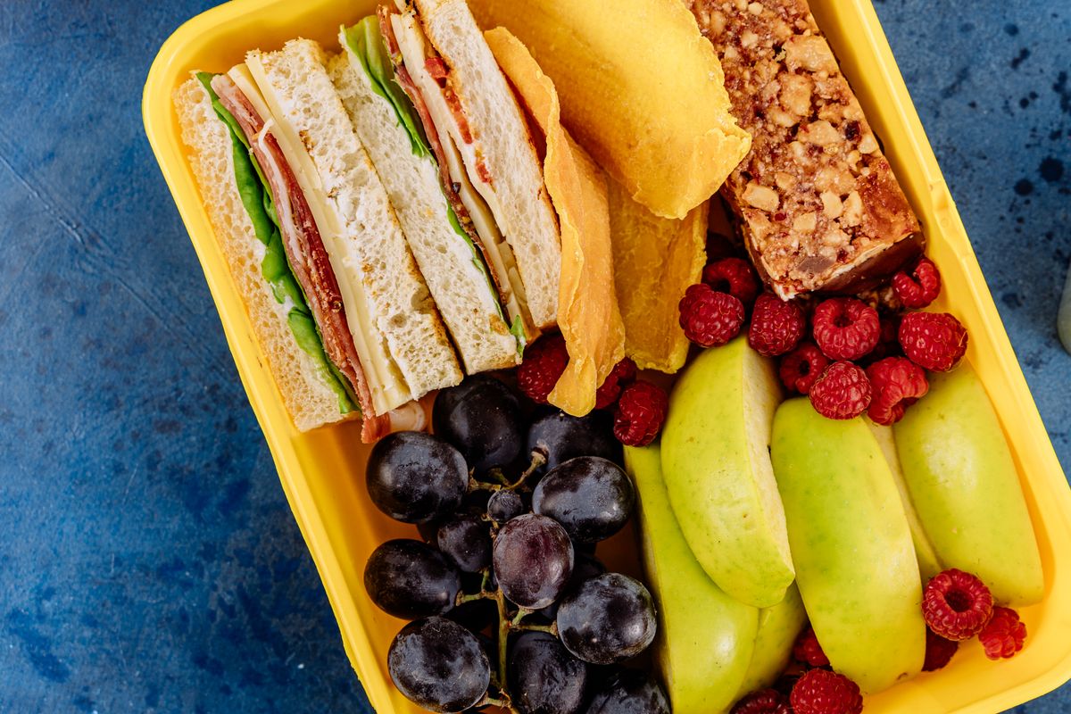 A packed lunch box with fruit, crackers, and a sandwich
